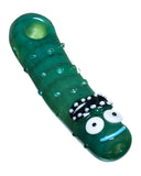 Diagonal view of Empire Glassworks Pickle Rick Spoon Pipe, which is a green pipe with glass bumps to represent a pickle. There is also a Rick face on the mouthpiece end of pipe. The pipe is displayed on a white background.